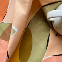 Load image into Gallery viewer, A close up of the coral coloured tea towel featuring an abstract leaf pattern There is a coffee cup sat on the tea towel.