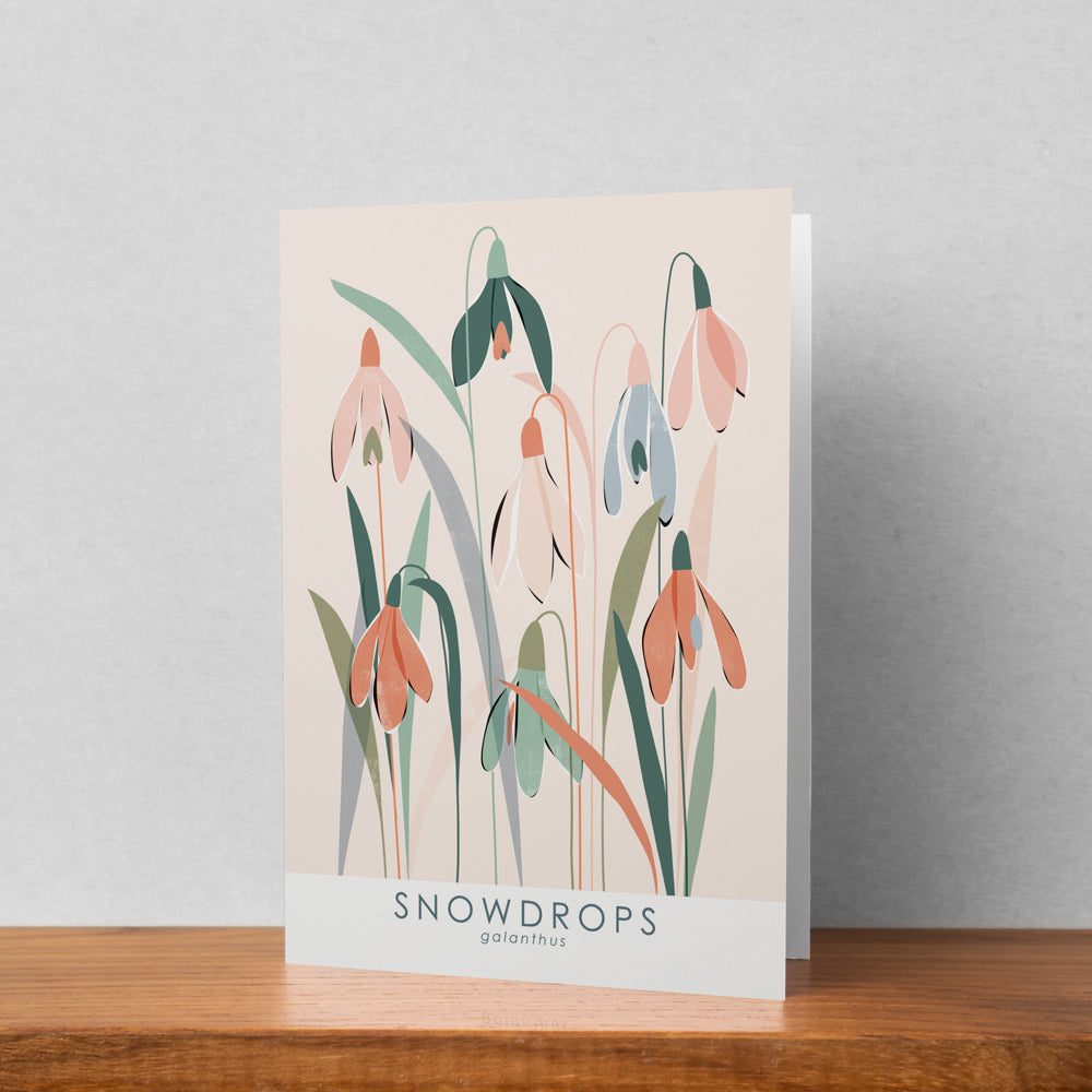 A greeting card featuring a snowdrops illustration stood up against a pale background. The text on the illustration reads snowdrops galanthus