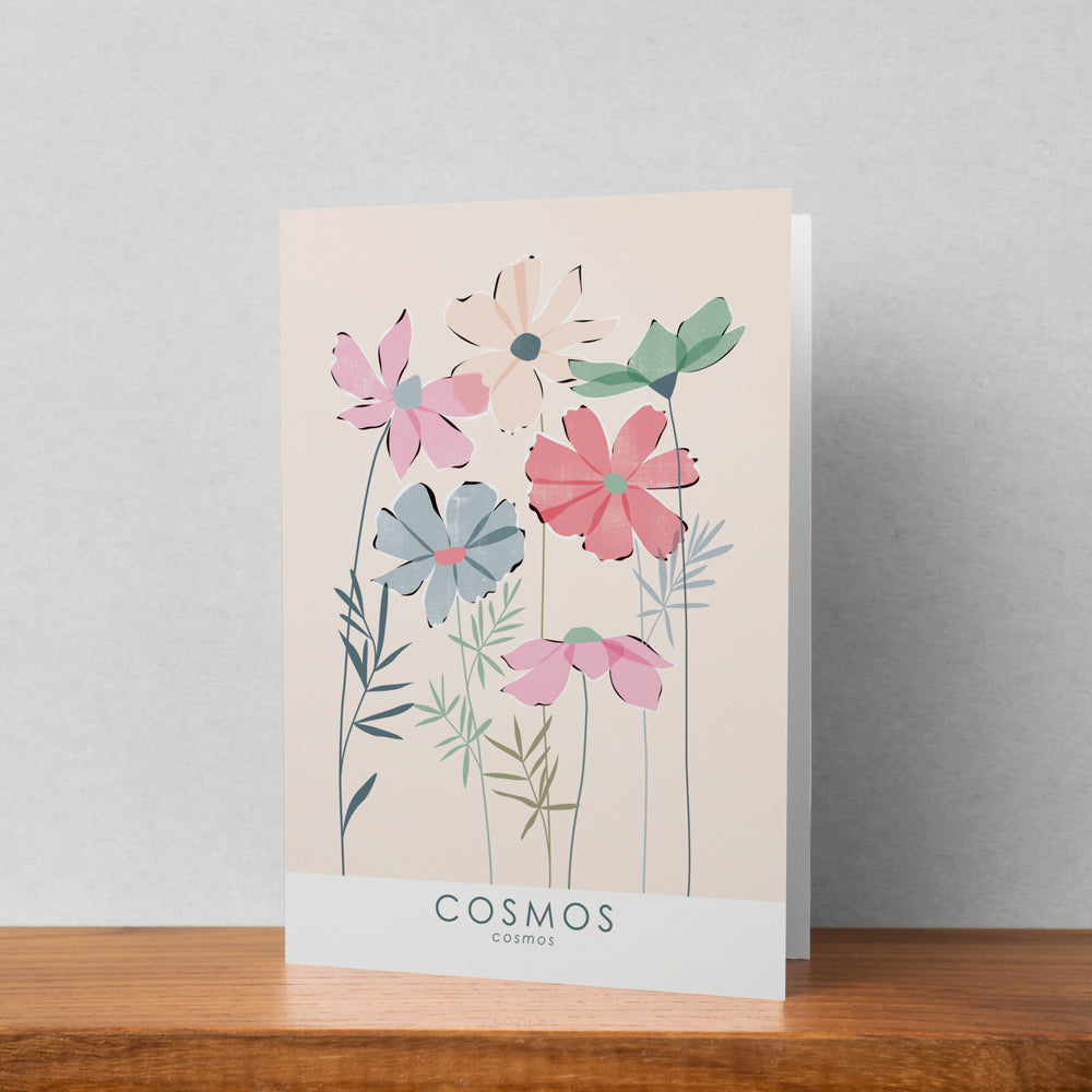 A greeting card featuring a cosmos illustration stood up against a pale background. The text on the illustration reads cosmos cosmos