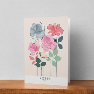 A greeting card featuring a roses illustration stood up against a pale background. The text on the illustration reads roses rosa